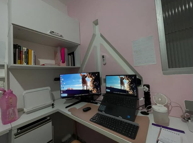 Cantinho de estudos da Pâmela, com dois monitores e estante de livros