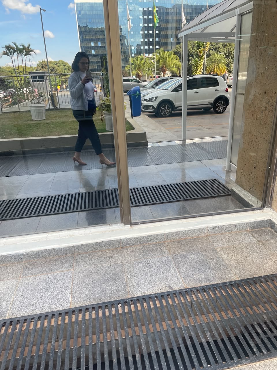 Reflexo da Pâmela caminhando na entrada do prédio da Justiça Federal, em um dia de céu azul