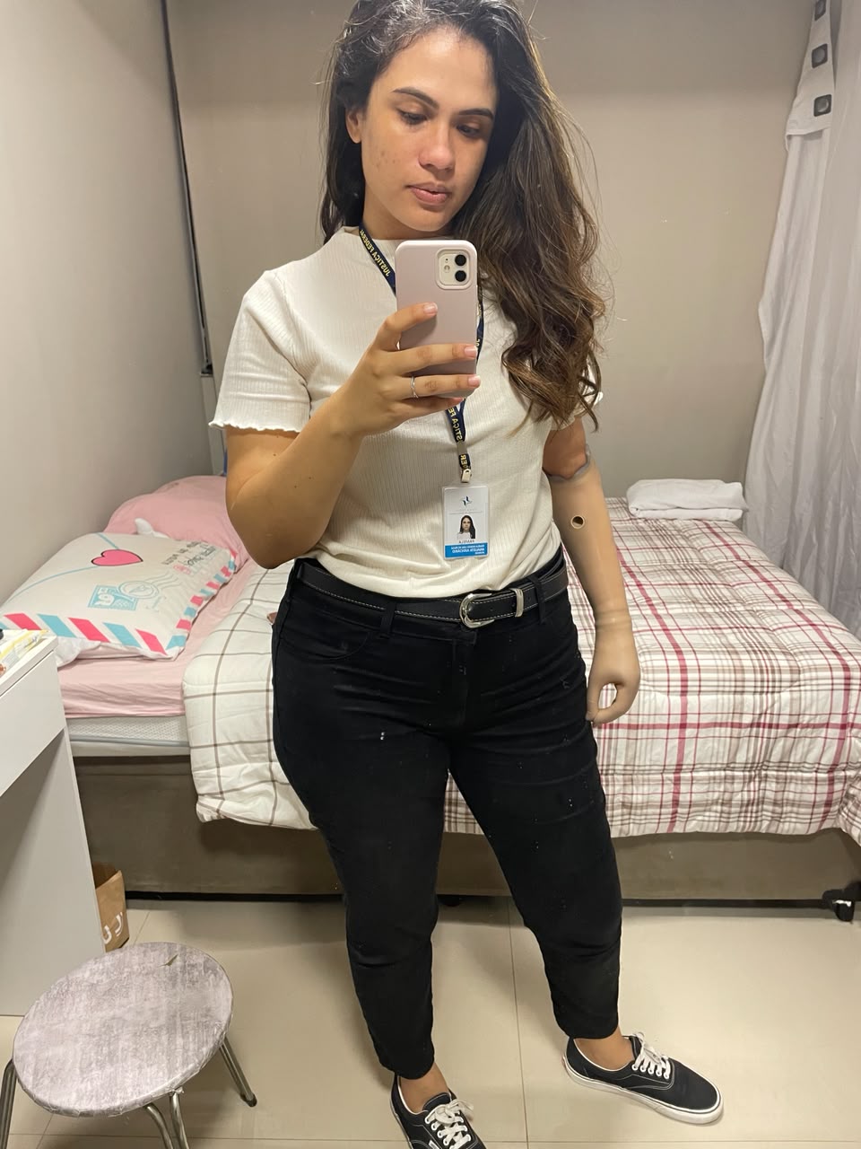 Pâmela em frente ao espelho com o crachá da Justiça Federal, camiseta branca, calça preta e tênis