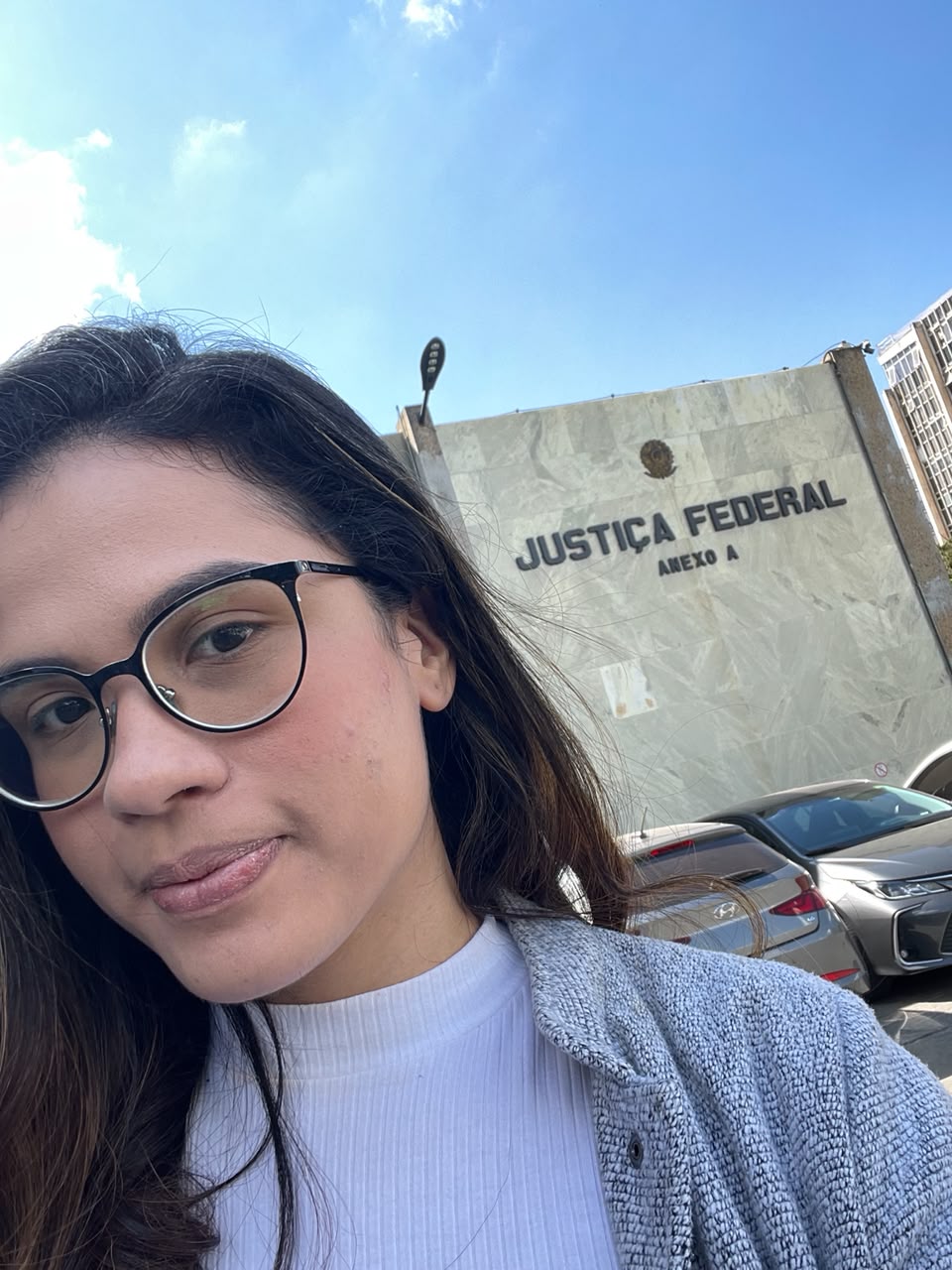 Pâmela sorrindo em frente ao prédio da Justiça Federal, com o letreiro do Anexo A ao fundo